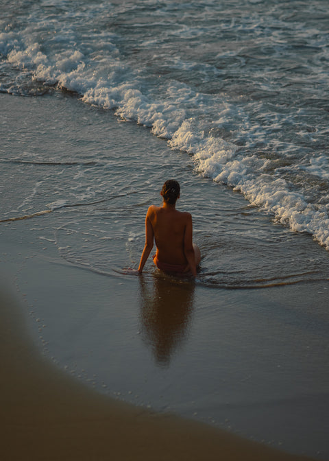 Frau sitzt am Meer mit warmen Farben und Wellen im Hintergrund